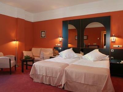 Doppelbettzimmer mit orangen Wänden, zwei Nachttischen, Sessel und Sofa mit Kissen.