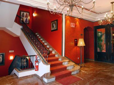 Rotes Treppenhaus mit goldenen Handläufen, braunem Fliesenboden und Kronleuchtern an weißer Decke.