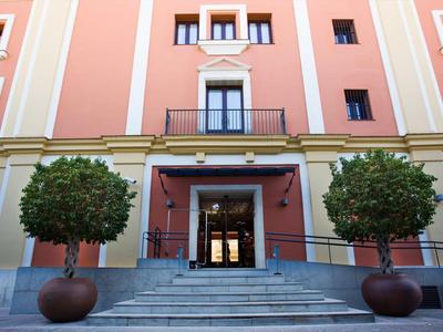 Eingang eines rosa Hauses mit Treppe, zwei großen Blumentöpfen und symmetrischen Fenstern.