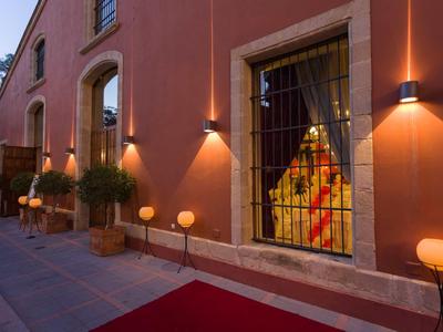 Rotes Gebäude mit beleuchteten Fenstern, dekorativen Kugellampen und Pflanzentöpfen am Gehweg.
