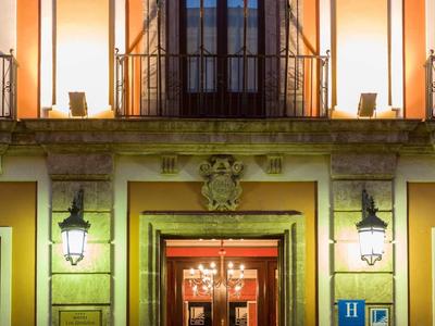 Eingang eines Gebäudes mit großen Türen, Laternen und warmem Licht bei Nacht.