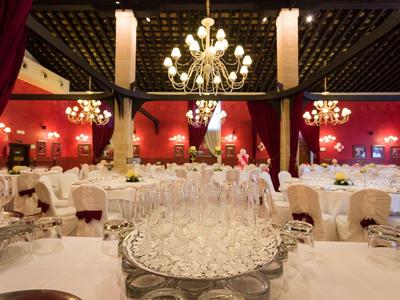 Eleganter Festsaal mit roten Wänden, weißen gedeckten Tischen und großen Kronleuchtern.