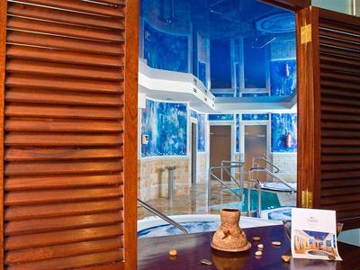 Blick durch offene braune Holzläden in einen hellen Raum mit Pool, blaue Wände und weiße Decke.