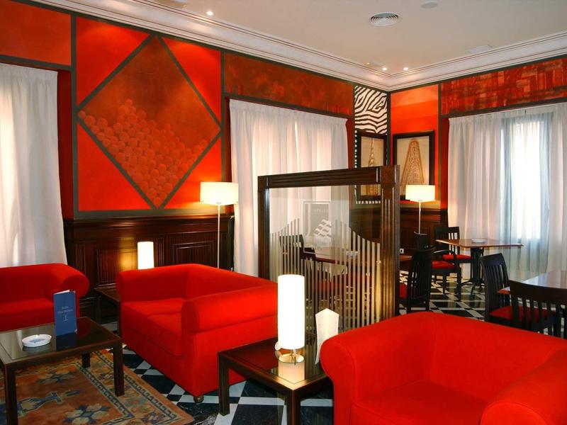 Wohnzimmer mit roten Sesseln, dunklem Holz, Teppich und großen Fenstern mit weißen Vorhängen.