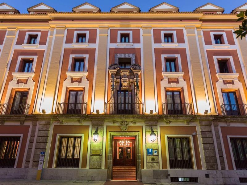 Beleuchtetes mehrstöckiges Gebäude mit symmetrischen Fenstern und dekorativen Fassadenelementen bei Nacht.