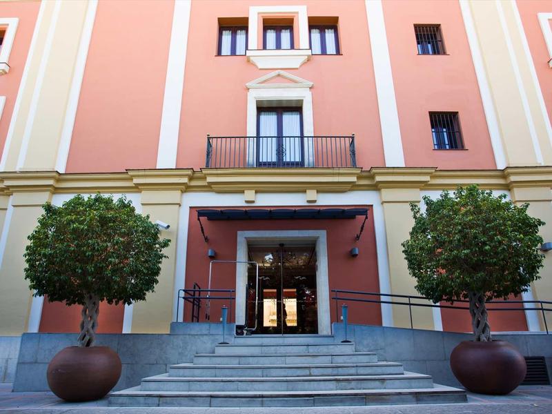 Eingang eines rosa Hauses mit Treppe, zwei großen Blumentöpfen und symmetrischen Fenstern.