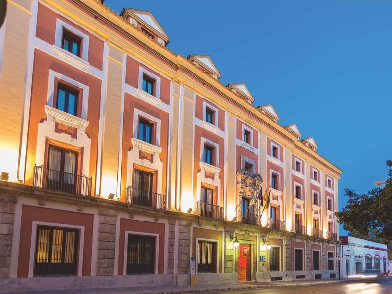 Beleuchtetes historisches Gebäude mit mehreren Fenstern und blauem Abendhimmel.