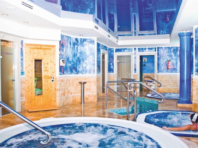 Moderner Wellnessbereich mit Whirlpool, Sauna, blauen Wänden und gläsernen Trennwänden.