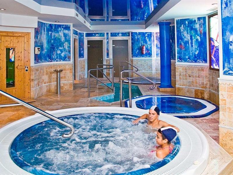 Zwei Personen entspannen im runden Whirlpool in einem hellen, modernen Wellnessbereich mit blauen Wandbildern.