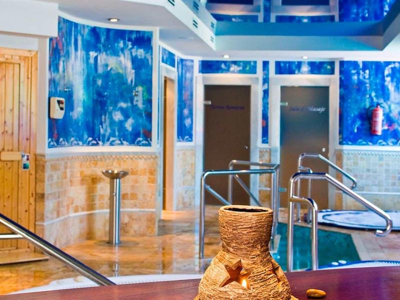 Hallenbad mit blauer Beleuchtung, Edelstahlgeländern und dekorativer Wandgestaltung.