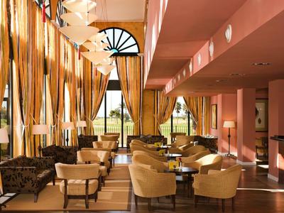 Eleganter Frühstücksraum mit gelben Sesseln, braunen Sofas, großen Fenstern und goldenen Vorhängen.