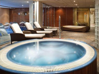 Moderne Wellness-Lounge mit rundem Whirlpool, Liegestühlen, Holz- und Glaswänden, sanfter Beleuchtung.