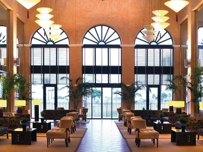 Großer heller Raum mit hohen Rundfenstern, gemütlichen Sitzgruppen und Pflanzen an den Wänden.