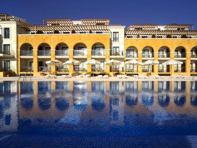 Großes gelbes Gebäude mit Rundbögen, Terrasse und blauem Schwimmbecken im Vordergrund.