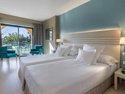 Modernes Hotelzimmer mit zwei großen Betten, blauen Sesseln und Balkon mit Meerblick.