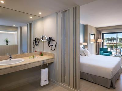 Modernes Hotelzimmer mit Doppelbett, Schreibtisch, Balkon und hell beleuchtetem Badezimmer.