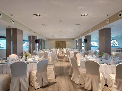 Großer eleganter Bankettsaal mit rund gedeckten Tischen und weißen Stuhlbezügen bei Tageslicht.