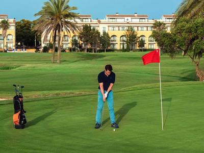 Golfer in blauer Hose bereitet Schlag auf dem Grün mit roter Fahne vor