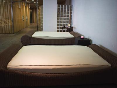 Zwei Massagebetten mit weißen Auflagen in einem ruhigen, schlichten Raum mit grauem Boden.