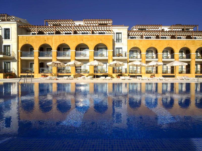 Großes gelbes Gebäude mit Rundbögen, Terrasse und blauem Schwimmbecken im Vordergrund.