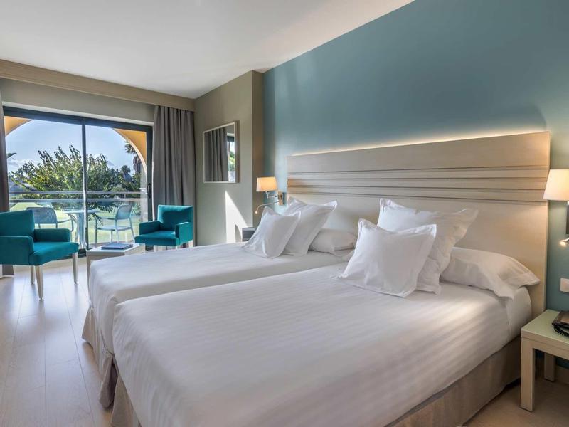 Modernes Hotelzimmer mit zwei großen Betten, blauen Sesseln und Balkon mit Meerblick.