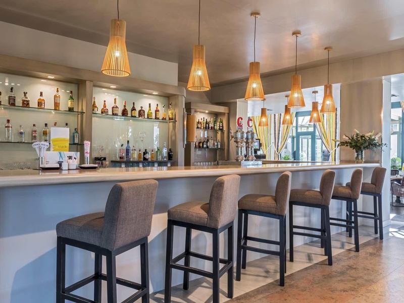 Moderner Barbereich mit langen Tresen, grauen Barhockern und hängenden gelben Lampen.