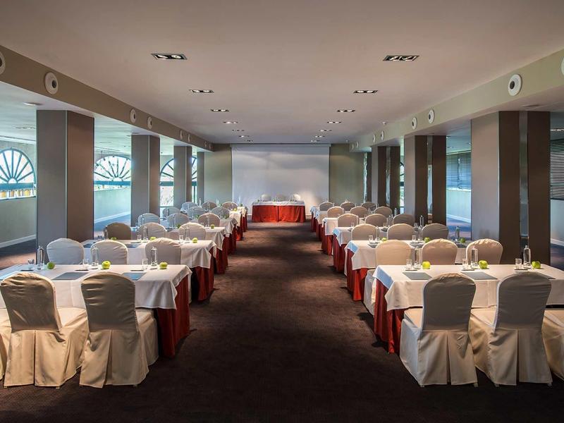 Großer Konferenzraum mit weißen Stuhlbezügen, langen Tischen und rotem Teppichmuster.