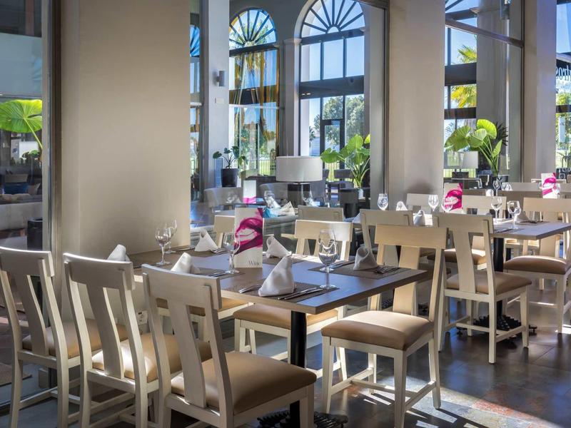 Hell eingerichtetes Restaurant mit Holzstühlen, großen Fenstern und modernem Ambiente.