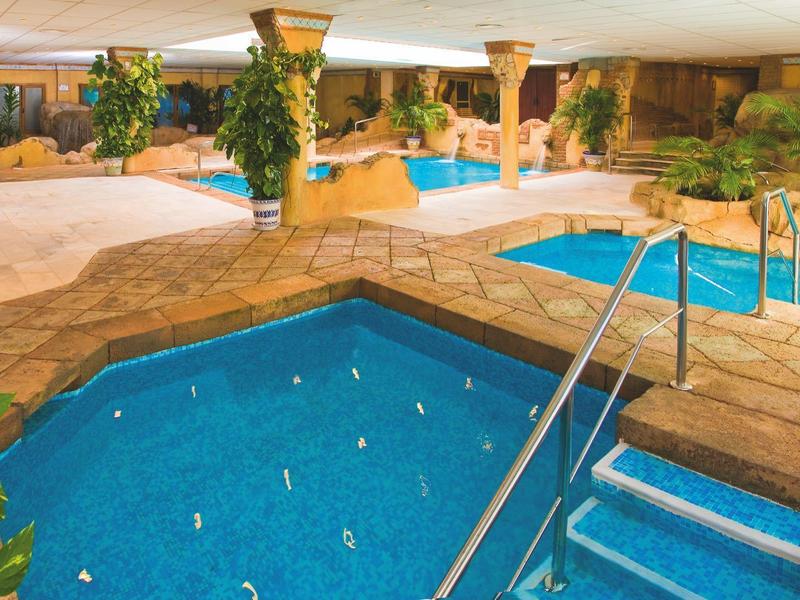 Innen-Schwimmbad mit drei unterschiedlich hohen Becken, Natursteinboden und grünen Pflanzen.