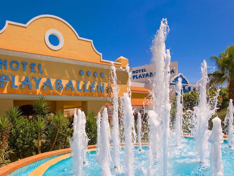 Hotel Playa Blanca mit gelb-orangefarbenem Gebäude und springenden Wasserspielen im Vordergrund.