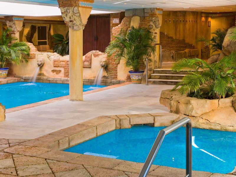 Innenpoolbereich mit zwei Pools, steiniger Umrandung und tropischen Pflanzen in warmem Licht.