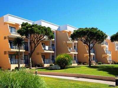 Mehrstöckige, beige Wohnungen mit Balkonen, umgeben von grünen Bäumen und gepflegtem Rasen.