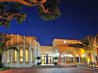 Modernes, beleuchtetes Gebäude mit großen Fenstern und Palmen bei Nacht.