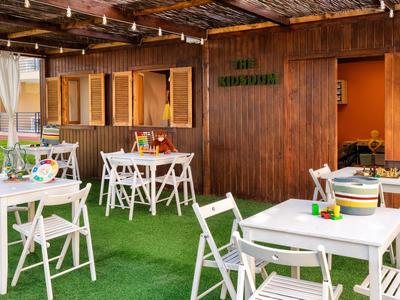 Gemütlicher Outdoor-Bereich mit weißen Stühlen und Tischen auf grünem Teppich vor Holzhaus