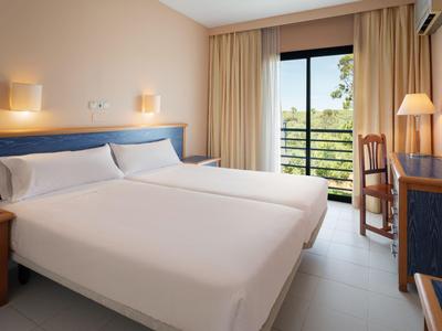 Hell eingerichtetes Hotelzimmer mit zwei Einzelbetten, Balkon und Schreibtisch.