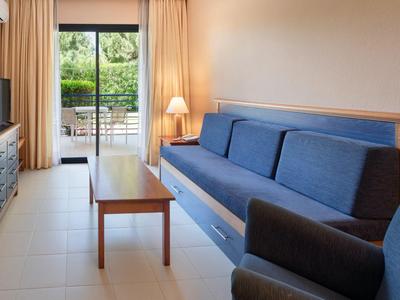 Helles Hotelzimmer mit blauem Sofa, Tisch und Terrasse mit Gartenblick.