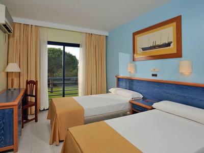 Zweibettzimmer mit blauen Wänden, weißen Betten, Holzmöbeln und Blick auf grüne Landschaft.