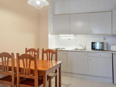 Kleine Küchenzeile mit weißen Schränken, Esstisch aus Holz und vier Stühlen in einem Hotelzimmer.