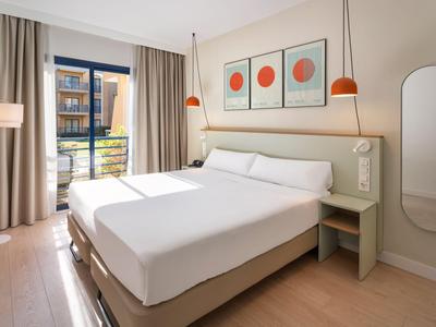 Helles Hotelzimmer mit Doppelbett, modernen Möbeln und Balkon mit Blick auf den Innenhof.