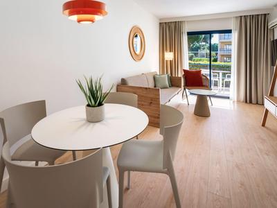 Moderner Hotelwohnraum mit Esstisch, Stühlen, Sofa, großem Fenster und Blick auf grüne Landschaft.