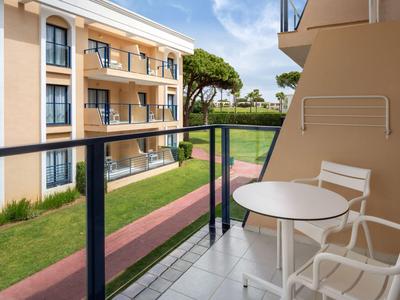 Balkon mit zwei weißen Stühlen und Tisch, Blick auf Hotelgebäude und Garten mit Weg