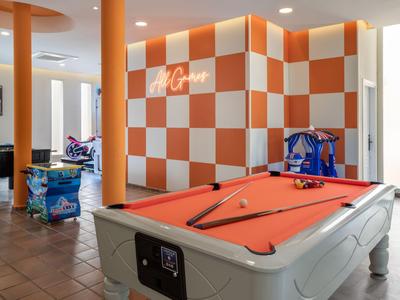 Hell beleuchteter Spielraum mit Billardtisch, Tischfußball und orange-weiß karierten Wänden.