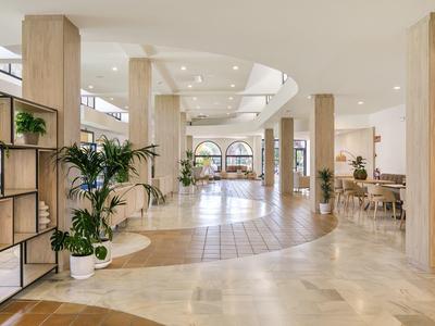 Heller, offener Innenraum mit großen Säulen, Pflanzen und Sitzbereichen in warmen Erdtönen.