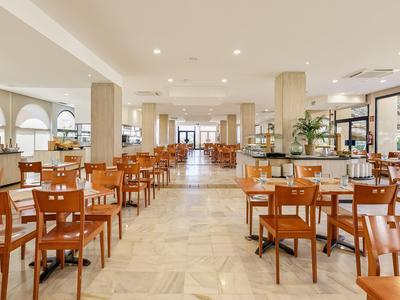 Helles, modernes Restaurant mit Holzstühlen, hellen Marmorböden und großen Fenstern.