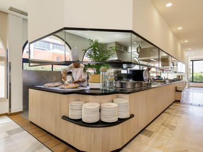 Modern ausgestattete Hotelküche mit Koch unter einer Haube und hellem Holzinterieur.