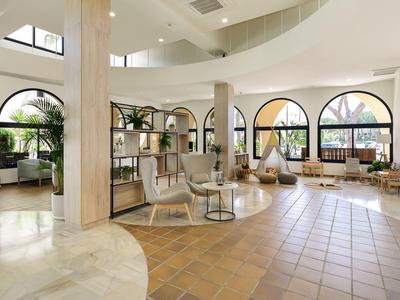 Helles Hotel-Lounge mit großen Fenstern, modernen Sitzgelegenheiten und Pflanzen.