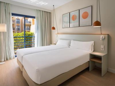 Modernes Hotelzimmer mit zwei Einzelbetten, großem Fenster und minimalistischer Dekoration.