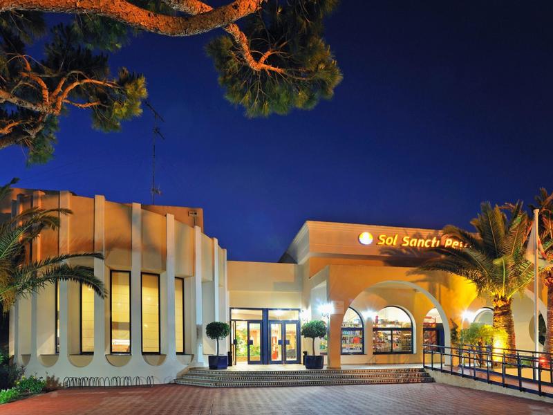 Modernes, beleuchtetes Gebäude mit großen Fenstern und Palmen bei Nacht.