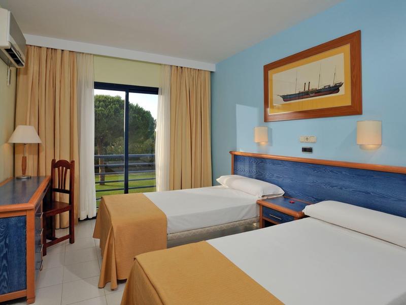 Zweibettzimmer mit blauen Wänden, weißen Betten, Holzmöbeln und Blick auf grüne Landschaft.