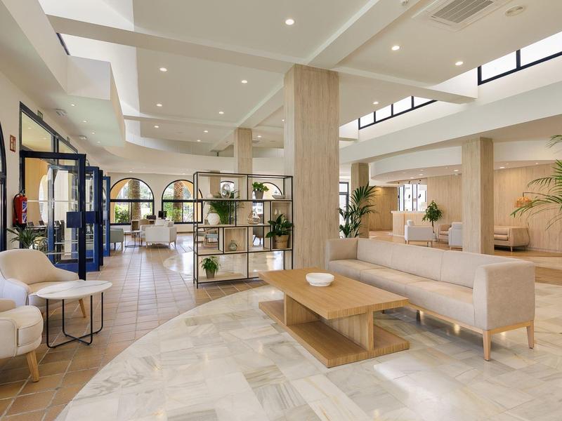 Helle, moderne Lobby mit beiger Einrichtung, Holzdetails und großen Fenstern für viel Tageslicht.